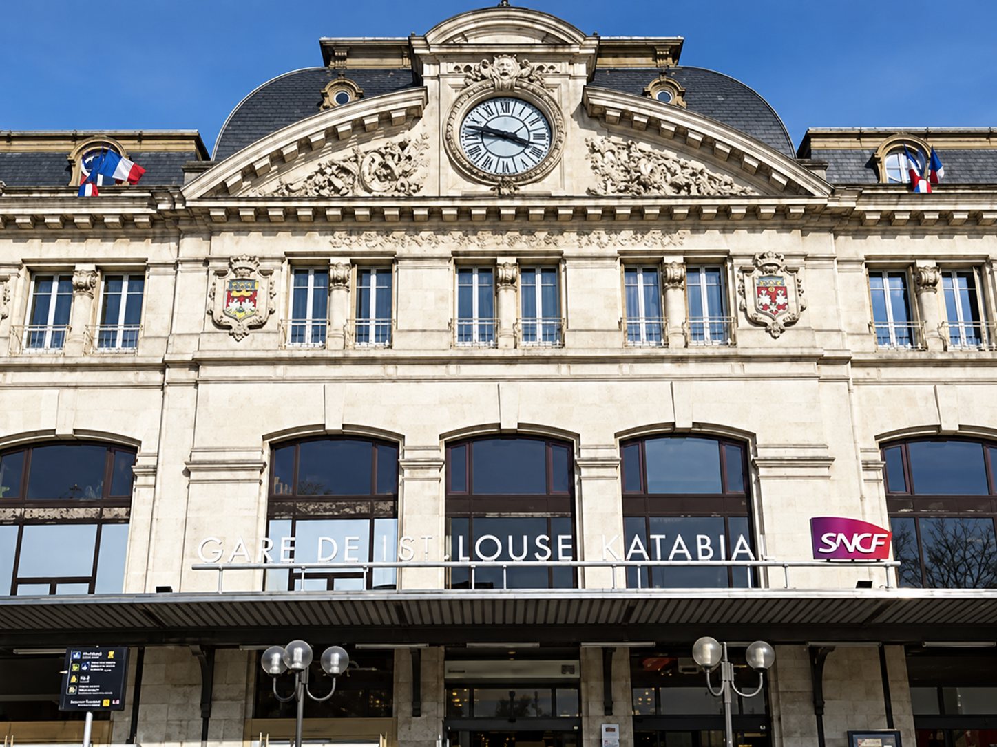 La façade en pierre claire d’une gare ancienne, surmontée d’une grande horloge et d’un dôme, avec le logo SNCF au-dessus des arcades vitrées.